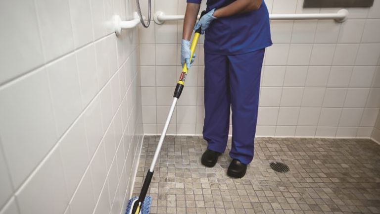 A Person cleaning an area on the Bathroom using HYGEN™ PUlSE™ Microfibre Mop Kit