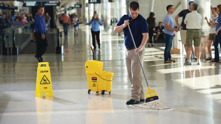 A cleaning personnel sweeping an airport flooring using WaveBrake® 33L Side Press Bucket and Wringer, "Caution Wet Floor" Sign and Rough Surface Wet Mop