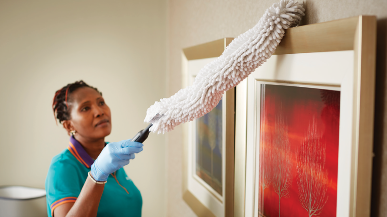 A worker at Amana Living cleaning the wall frames with HYGEN™ Quick-Connect Flexi-Wand With Microfibre Dusting Sleeve