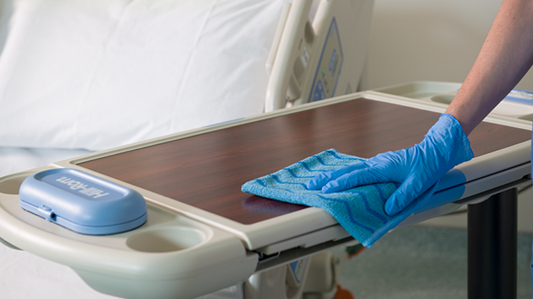 A person cleaning a hospital bedside table with a Blue HYGEN™ Microfibre Cloth