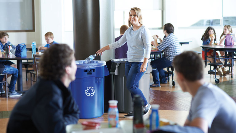 Woman throwing a plastic bottle on a Rubbermaid® BRUTE 32 Gallon Blue Round Recycling Can