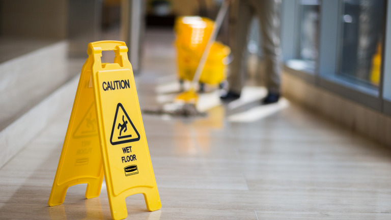 Wet floor caution sign next to a mop, informing people of a wet surface.